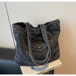 Close-up of black denim tote bag with white contrast stitching and front flap pocket detail