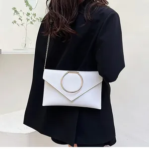 Détail d'une pochette enveloppe blanche avec boucle dorée en anneau et bandoulière chaîne