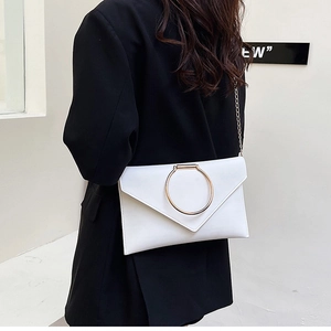 Pochette enveloppe blanche élégante avec boucle anneau dorée et chaîne sur tailleur noir