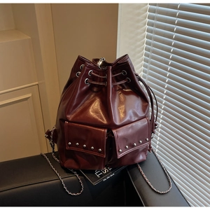 Detail of dark burgundy bucket bag with studded pockets and chain strap on leather surface