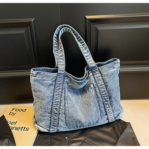 Close-up of blue washed denim tote bag with a large front pocket and thick shoulder straps