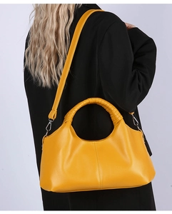 Detail of yellow pebbled leather handbag featuring curved top and模特 wearing black suit