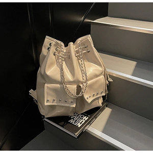 Detail of cream drawstring bucket bag with metal studs and double chain straps