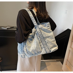 Side view of large light blue denim tote bag with functional front pockets on model