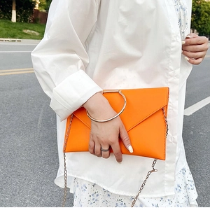 Détail d'une pochette enveloppe orange avec poignée ronde dorée et fine chaîne métal