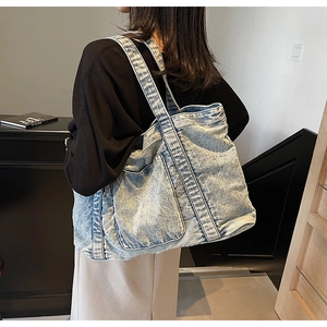 Detail of light blue washed denim tote bag showing texture and front pocket design