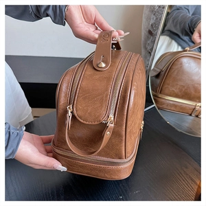 Detail view of large brown faux leather cosmetic bag with double zippers and top handle
