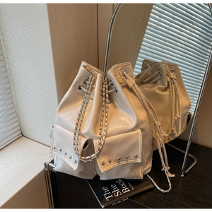 Detail view of cream drawstring bucket bag featuring silver rivets and chain strap