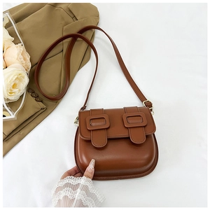 Détails du sac besace marron caramel avec boucles décoratives sur un fond minimaliste