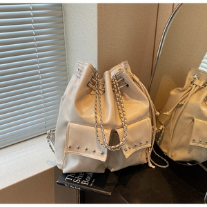 Detail of beige bucket backpack with silver rivets and metal chain straps on table