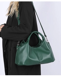 Detail of dark green pebble leather handbag with braided handle and adjustable shoulder strap