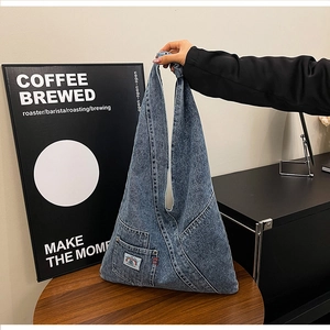 Detail of blue washed denim tote bag featuring utility pocket and woven logo label