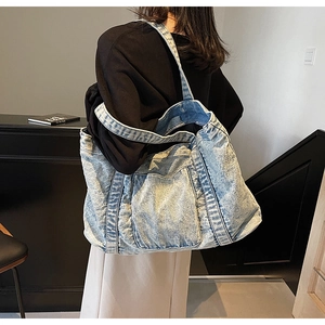 Detailed side view of a large vintage blue denim tote bag worn by a model