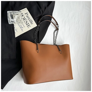 Flat lay of brown leather tote bag with metal chain straps on elegant white fabric
