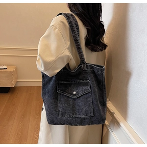 Detail of vintage denim tote bag with front pocket and silver buckle worn on shoulder