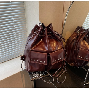 Detail of dark brown rivet bucket bag with drawstring closure and metal chain strap