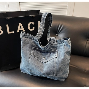 Close-up of vintage denim tote bag with front pocket and metal buckle on black sofa
