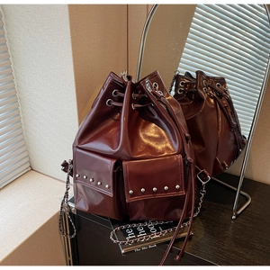 Detail of burgundy leather bucket bag featuring silver rivets and drawstring closure