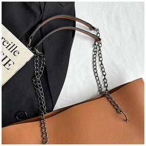 Detail of a brown tote bag with metal chain straps and pebble grain leather texture