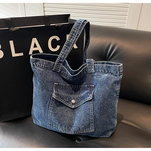 Detail of blue denim tote bag with front flap pocket on black leather sofa