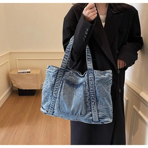 Detail of vintage blue washed denim tote bag with front pocket shown on a model