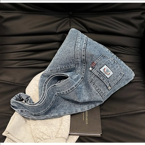 Detailed close-up of washed denim shoulder bag with woven label on black leather surface