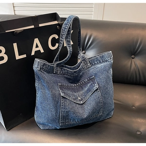 Close-up of vintage blue denim tote bag with front pocket detail on black leather sofa