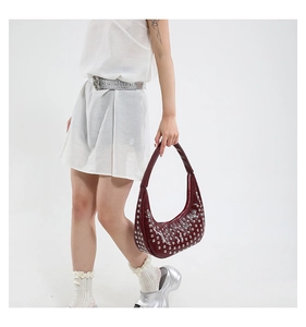 Detail der burgunderroten Ledertasche mit silbernen Punk-Nieten von einem Model gehalten