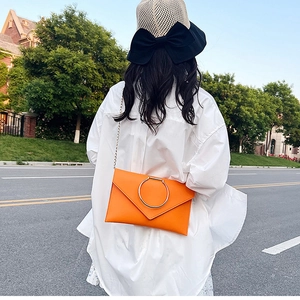 Détail d'une pochette enveloppe orange avec un grand anneau métallique et une chaîne