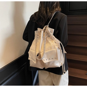 Detail of creamy white bucket backpack featuring glossy finish, metal rivets and chain strap