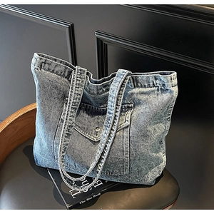 Close-up detail of light blue washed denim tote bag with front flap pocket and metal button