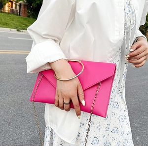 Gros plan d'une pochette enveloppe rose fuchsia avec poignée anneau dorée et chaîne