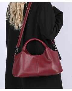 Detail view of burgundy pebble leather handbag with round handles and adjustable shoulder strap