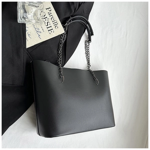 Detail of minimalist black tote bag with matte leather texture and metal chain handles