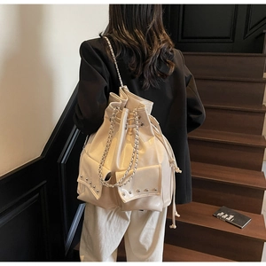 Detail of off-white bucket bag featuring drawstring closure, silver rivets, and chain strap