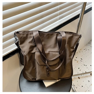 Deep brown nylon tote bag with metal chain detail and spacious front pocket on a black stool