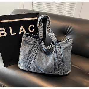 Detailed close-up of large denim tote bag with front pocket on a black leather sofa