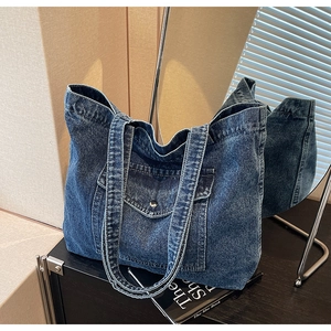 Detail of dark blue denim tote bag showing wide shoulder straps and front flap pocket