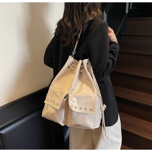 Detail of a creamy white bucket bag featuring silver rivet pockets and a shiny PU finish