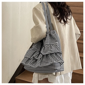 Detail of checkered tote bag with tiered ruffles and dual straps on light blazer