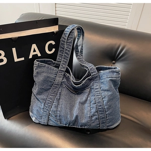 Close-up of vintage blue denim tote bag with front pocket on a black leather sofa