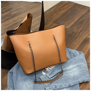 Detail of vintage brown leather tote bag with black chain strap on denim jacket