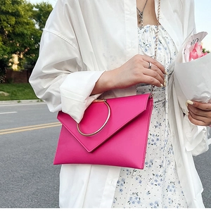 Détail du sac enveloppe en cuir rose rouge avec poignée anneau dorée et chaîne