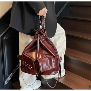 Detail of burgundy bucket bag with silver studs and chain handle on wooden stairs