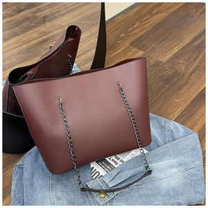 Detail of burgundy leather tote bag with metal chain strap on denim jacket and wood floor