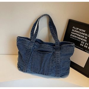 Detailed close-up of blue washed denim tote bag with visible stitching and front pocket