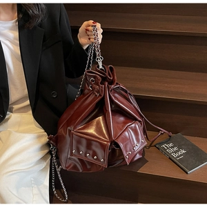 Detail of dark red drawstring bucket bag with silver studs and chain strap held by model