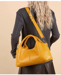 Detail view of yellow leather handbag with woven handle and adjustable strap on a model