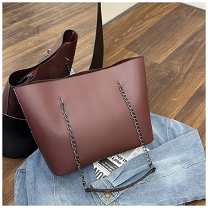 Detail of burgundy tote bag with chain strap resting on denim and wood background