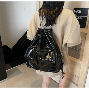 Detail of glossy black rivet bucket bag featuring silver chain straps and drawstring closure